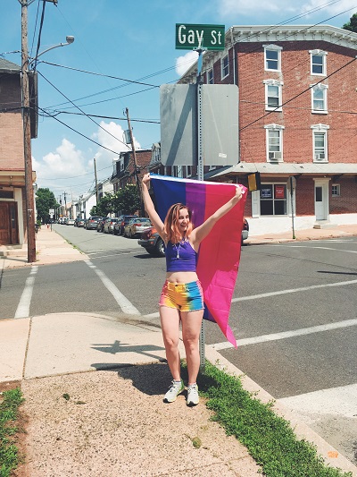 picture of me holding a bi pride flag in front of a street sign that reads "Gay Street"